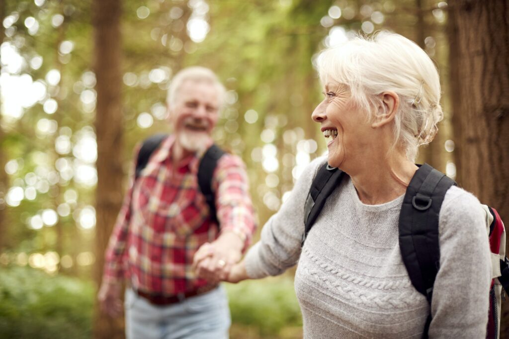 Loving Retired Senior Couple Holding Hands Hiking In Woodland Countryside Together